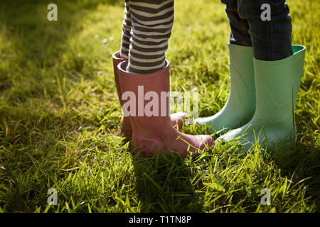 Niedrigen Winkel zuschneiden und seitlichem Blick auf zwei Kinder tragen Gummistiefel und stehen auf Sommer Gras Stockfoto