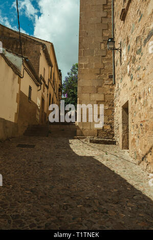 Schmale Gasse mit Treppe inmitten von alten Steinmauern an einem sonnigen Tag in Caceres. Eine charmante Stadt mit einem vollständig erhaltenen Altstadt in Spanien. Stockfoto