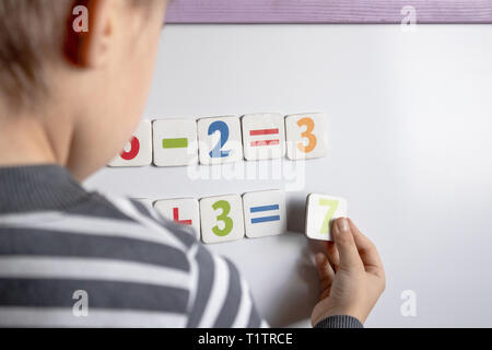 Ein kleiner Junge löst eine schwierige Aufgabe. Vor dem Hintergrund der School board mit Zahlen in ihre Hände und zählt Beispiele. Stockfoto