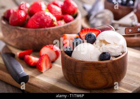 Vanilleeis mit frischen Blaubeeren und Erdbeeren in eine hölzerne Schüssel mit Schalen der Beeren im Hintergrund Stockfoto