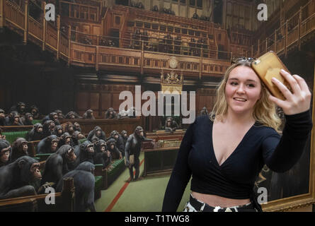 Isabelle Schofield nimmt ein Foto von sich vor dem Gemälde 'Dentwickelte sich das Parlament durch die Graffiti Künstler Banksy, der auf der Bristol Museum ist. Stockfoto