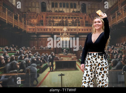 Isabelle Schofield nimmt ein Foto von sich vor dem Gemälde 'Dentwickelte sich das Parlament durch die Graffiti Künstler Banksy, der auf der Bristol Museum ist. Stockfoto