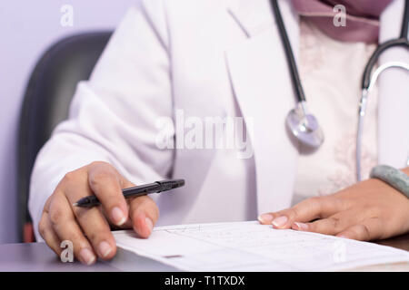 Hijab Ärztin hand Schreiben auf ein Papier für den Eingang auf Ihrem Schreibtisch im Innenbereich Stockfoto