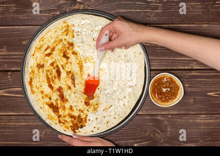 Frau Hand ist die Tomate sause. Rezept Schritt für Schritt Pizza Capricciosa flatlay auf braunem Holz Stockfoto