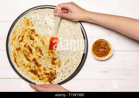 Frau Hand ist die Tomate sause. Rezept Schritt für Schritt Pizza Capricciosa flatlay auf weißem Holz Stockfoto