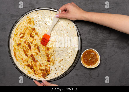 Frau Hand ist die Tomate sause. Rezept Schritt für Schritt Pizza Capricciosa flatlay am grauen Stein Stockfoto