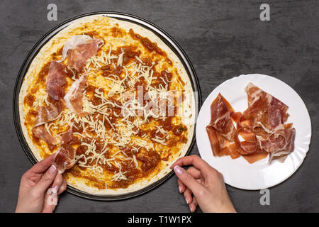 Setzen Sie Stücke von jamon auf eine Pizza. Rezept Schritt für Schritt Pizza Capricciosa flatlay am grauen Stein Stockfoto