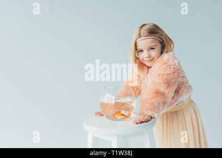 Cute kid in Fellimitat Mantel und Rock mit FISHBOWL an Kamera isoliert auf Grau suchen Stockfoto