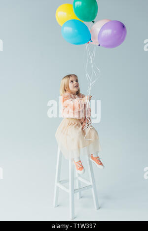 Cute kid in Fellimitat Mantel und Rock sitzt auf Hochstuhl und Holding Ballons Stockfoto