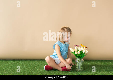 Glückliches Kind Sitzen mit gekreuzten Beinen und mit Blick auf die Blumen und Schmetterlinge Stockfoto