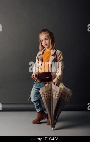 Kind in Trenchcoat und Jeans mit Regenschirm und Wegsehen Stockfoto
