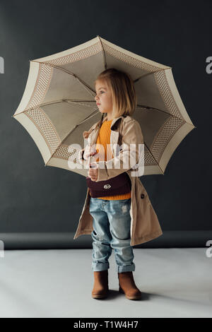Schwere Kind in Trenchcoat und Jeans mit Regenschirm und Wegsehen Stockfoto