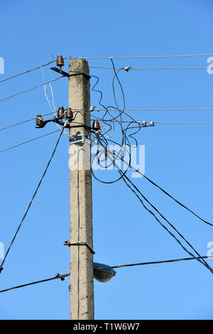 Schließen Sie den oberen Teil des Utility Pole mit vielen elektrischen Drähten und Isolatoren in hellen Morgen Sonnenlicht auf blauen Himmel Hintergrund. Stockfoto