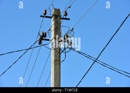 Schließen Sie den oberen Teil des Utility Pole mit vielen elektrischen Drähten und Isolatoren in hellen Morgen Sonnenlicht auf blauen Himmel Hintergrund. Stockfoto