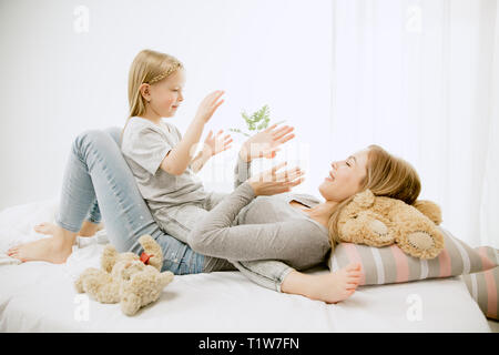 Junge Mutter und ihre kleine Tochter zu Hause am sonnigen Morgen. Weiche Pastellfarben. Happy Family Zeit am Wochenende. Muttertag Konzept. Familie, Liebe, Lifestyle, Mutterschaft und zärtliche Momente Konzepte. Stockfoto