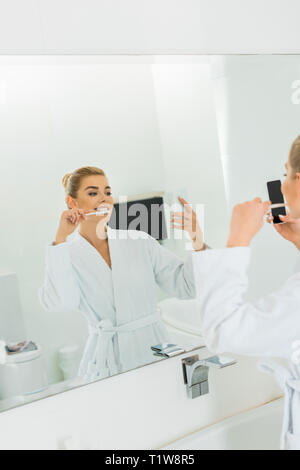 Selektiver Fokus der Frau in weiß Bademantel Zähneputzen und die selfie Stockfoto