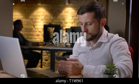 Closeup Schießen von Erwachsenen kaukasischen Geschäftsmann mit dem Telefon vor dem Laptop zuhause im Büro Stockfoto