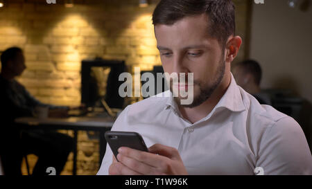 Closeup Schießen von Erwachsenen kaukasischen Geschäftsmann Surfen auf das Telefon am Arbeitsplatz im Büro Stockfoto