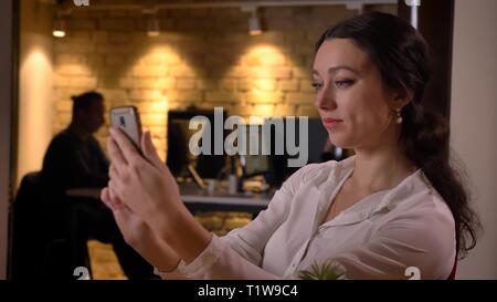 Closeup Schießen von jungen Hübschen kaukasischen Geschäftsfrau unter selfies am Telefon, während Sitzen vor dem Laptop zuhause am Arbeitsplatz Stockfoto