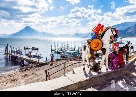 Panajachel, Atitlan See, Guatemala - 8. März, 2019: Kunststoff Pferde für Kinder Fotos am Strand mit Stegen, angelegte Boote & 3 Vulkane Stockfoto