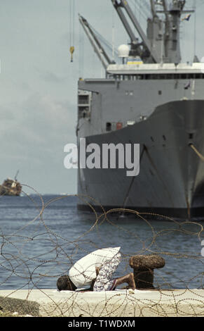29. Oktober 1993 Ein somalischer Mann betet in Richtung Mekka im neuen Hafen in Mogadischu, Somalia. Im Hintergrund steht das Vehicle Cargo Ship der United States Marine Administration, USNS Denebola, ein riesiges amerikanisches Marineschiff, das gerade Fahrzeuge entlädt. Ebenfalls im Hintergrund befindet sich das Wrack des rumänischen Frachtschiffes Felix an der Hafenmauer des alten Hafens. Stockfoto