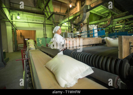 14. Oktober 2014. Der Ukraine Kiew. Die Frau des durchschnittlichen Jahren in einem weißen Bademantel arbeitet auf einem Fließband im Werk der Zeiten der Sowjetischen, manuellen Fähigkeiten Stockfoto