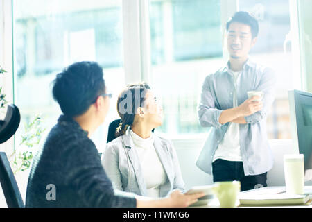 Drei junge asiatische Männer und Frauen Chatten in Büro, glücklich und entspannt. Stockfoto