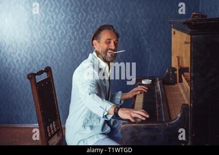 Brutaler Mann mit einem Bart, 40 Jahre alt, spielt das alte Klavier. Stockfoto