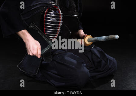 Ansicht des Kendo Kämpfer holding Helm und Bambus Schwert auf Schwarz 7/8 Stockfoto