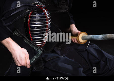 Ansicht des Kendo Kämpfer holding Helm und Bambus Schwert auf Schwarz 7/8 Stockfoto