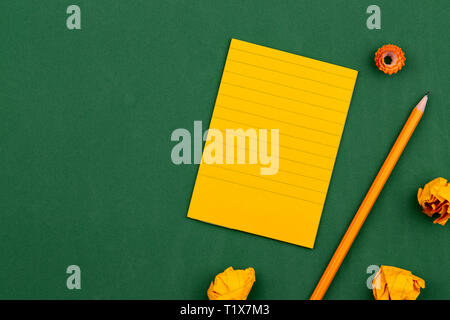 Eine orange Blatt Papier liegt auf einem grünen School Board bilden einen Rahmen für Text. in der Nähe von Stift und Zerknitterte Seiten. Kopieren raum Flache Ansicht von Oben Konz legen Stockfoto