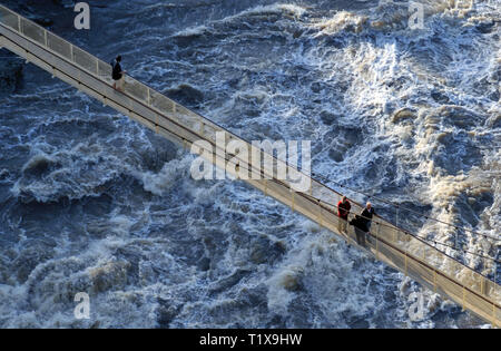 Einen erhöhten Blick auf drei Personen auf einer Hängebrücke auf den überschwemmten Tamar River in Launceston, Tasmanien, Australien. Stockfoto