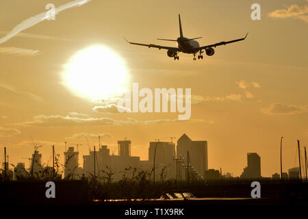 Flugzeug Landung am Flughafen London City mit goldenen Himmel, wie die Sonne hinter der Canary Wharf skyline Stockfoto