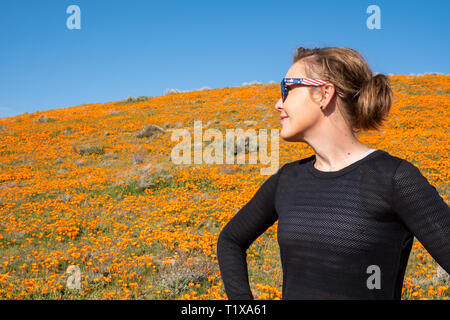 Glückliche Frau lächelt in die Ferne auf die helle orange Hügel mit Mohn gefüllt während des superbloom auf Antelope Valley Poppy Finden Suchen Stockfoto