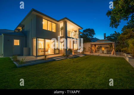 Dämmerung Blick auf moderne Große Australische home, mit Licht gefüllt Zimmer, Holzböden, Metall Geländer, Outdoor und Balkon unterhalten. Stockfoto