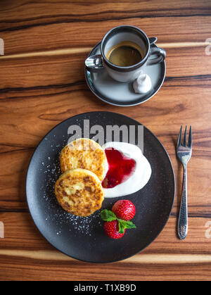 Quark Pfannkuchen und Kaffee. Russische syrniki mit Cranberry Marmelade und Joghurt, selektive konzentrieren. Stockfoto