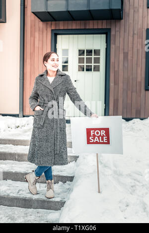 Schöne stilvolle Frau setzend für Verkauf Zeichen in der Nähe von Ihrem Haus Stockfoto