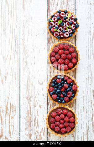 Himbeeren und Blaubeeren Törtchen mit Ganache, frische Beeren und Minze, selektiven Fokus. Frisches Obst Torte auf weißem Hintergrund, frisch Stockfoto