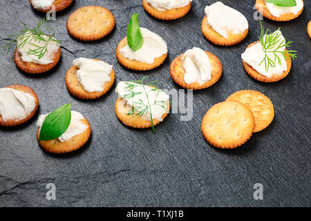 Ein Foto von Salz Cracker mit weichen Frischkäse und Kräutern auf einem schwarzen Hintergrund mit einem Platz für Text Stockfoto