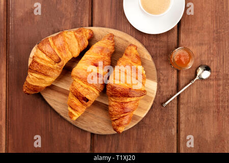 Ein Foto von Croissants, geschossen von oben auf einen dunklen Holzmöbeln im Landhausstil Hintergrund mit Kaffee, Marmelade, und einen Platz für Text Stockfoto
