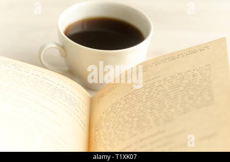 Eine Tasse Kaffee und ein offenes Buch auf weißem Holz- Hintergrund Stockfoto