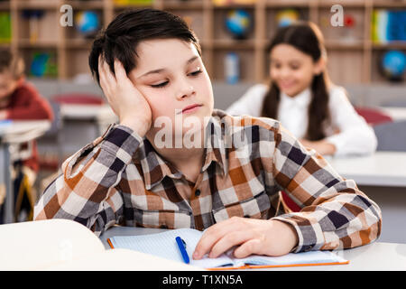 Verärgert Schuljunge mit Notebook am Schreibtisch sitzen im Klassenzimmer Stockfoto