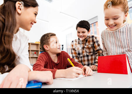 Lächelnd Schülerinnen und Schüler mit Notebooks und Bücher Diskutieren im Klassenzimmer Stockfoto