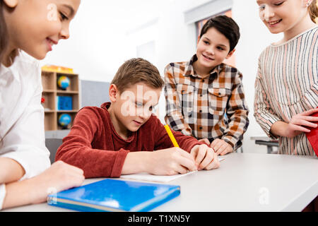 Lächelnd Schülerinnen und Schüler mit Notebooks und Bücher Diskutieren im Klassenzimmer Stockfoto
