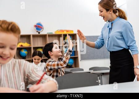 Lächelnd Lehrer und Schüler heben die Hände für hohe fünf im Klassenzimmer Stockfoto