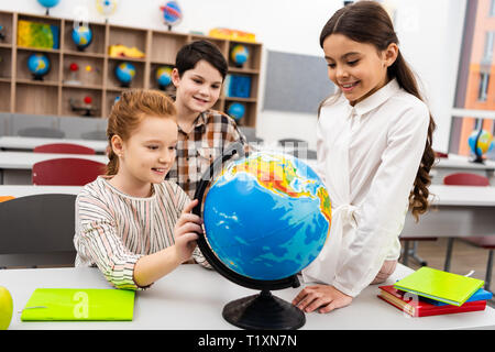 Drei fröhliche Schüler spielen mit Globe im Klassenzimmer während Geographie Lektion Stockfoto