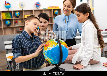 Lehrer und Schüler berühren Globus mit Lächeln während des Studiums Geographie im Unterricht Stockfoto