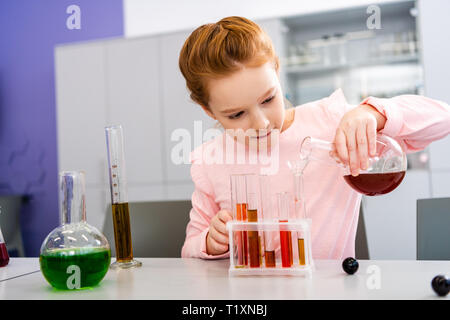 Lächelnd Schulmädchen holding Becher und chemischen Experiment während Chemie Lektion Stockfoto