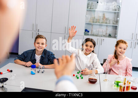 Lächelnd Schulmädchen anheben Hand in Klasse während Chemie Lektion Stockfoto