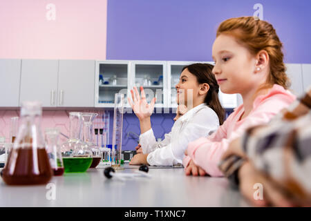 Lächelnd Schulmädchen anheben Hand in Klasse während Chemie Lektion Stockfoto